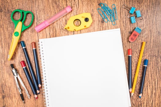 School accessories, pencil, pen, scissors, blank sheet of paper on a wooden desk. View from above
