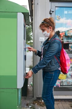 Woman buying bus ticket in ticket machine wearing face mask to cover mouth and nose traveling during pandemic coronavirus outbreak