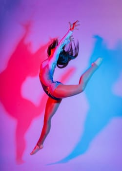 A girl gymnast in a swimsuit does tricks on white and dark background. Front view