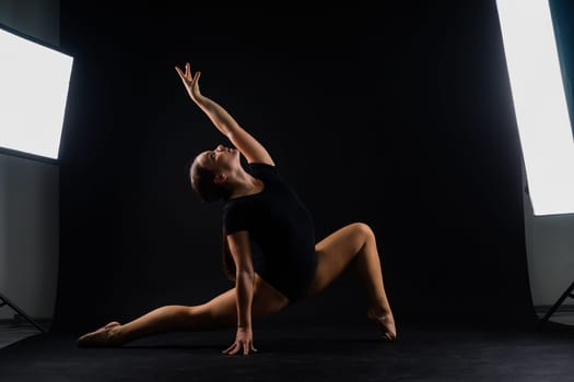 A girl gymnast in a swimsuit does tricks on white and dark background. Front view