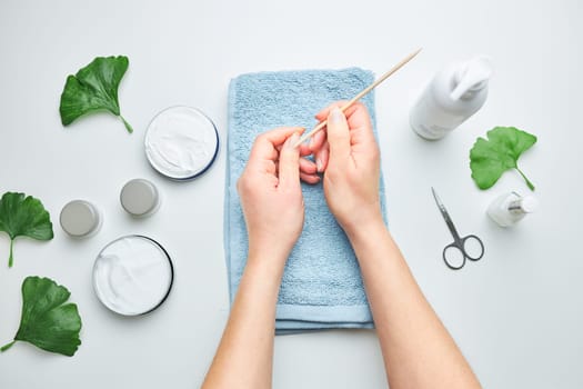 Woman applying  cosmetic moisturizing hand cream. Cosmetic products, green leaves on white table. Spa, manicure, skin care concept. Flat lay, overhead view