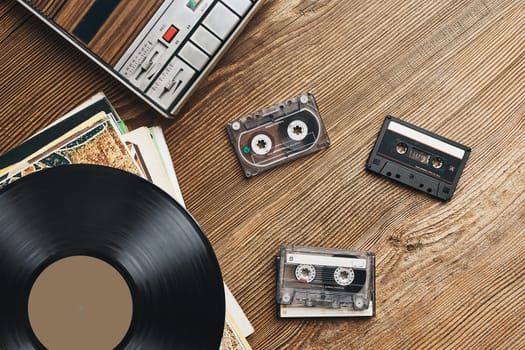 Vinyl records, cassette tapes and cassette recorder on wooden table. Retro music style. 80s music party. Vintage style. Analog equipment. Stereo sound. Back to the past