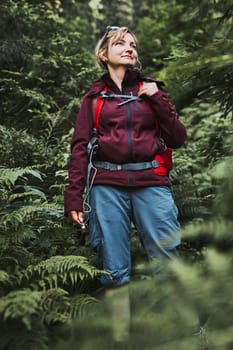 Woman with backpack hiking in forest, actively spending summer vacation close to nature. Woman walking on path among trees