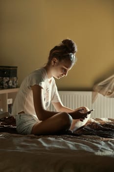 Young woman using portable computer and mobile phone, sitting on a bed, learning online at home. Candid people, real moments, authentic situations