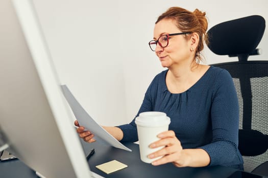 Woman entrepreneur reading financial data with satisfaction. Pleased happy business woman working in office sitting at desk using computer