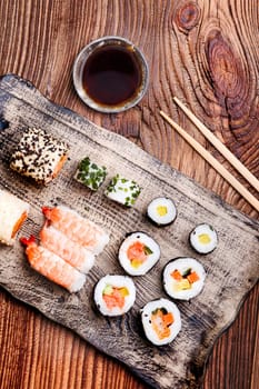 Sushi set on pottery plate with chopsticks and soy sauce in bowl on old wooden table from above