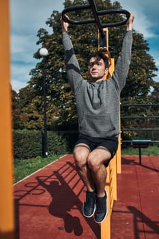 Young man bodybuilder exercising pulling up his legs during his workout in a modern calisthenics street workout park. Man wearing sportswear
