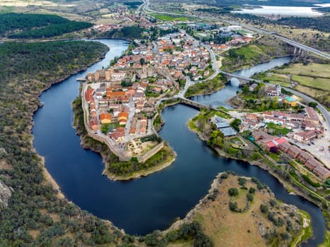 Aerial view of Buitrago del Lozoya, a well preserved historic village near Madrid, surrounded by the Lozoya river, with the Guadarrama mountain chain and reservoir in the background. Long exposure.