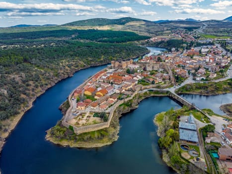 Aerial view of Buitrago del Lozoya, a well preserved historic village near Madrid, surrounded by the Lozoya river, with the Guadarrama mountain chain and reservoir in the background. Long exposure.