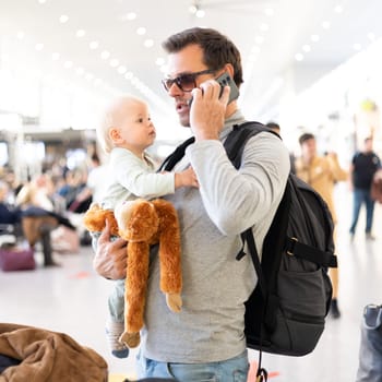Father traveling with child, holding his infant baby boy at airport terminal waiting to board a plane. Travel with kids concept