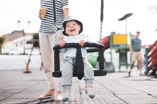 Mother pushing her infant baby boy child on a swing on playground outdoors