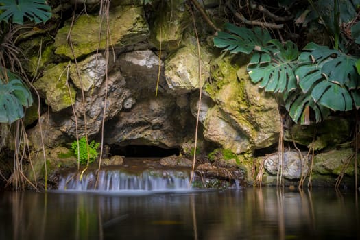 tropical garden pond with waterfall and rock wall, long exposure.
