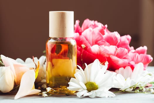 Beautiful flowers and clear glass bottle of yellow oil or perfume standing on gray surface