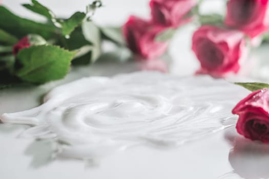 White cream smeared on glossy surface surrounded by blurred delicate pink roses