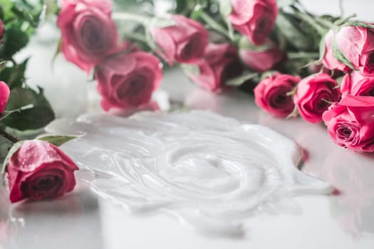 White cream smeared on glossy surface surrounded by blurred delicate pink roses