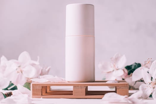 Antiperspirant roll-on deodorant on wooden podium in form of pallet on light plaster surface with apple flowers