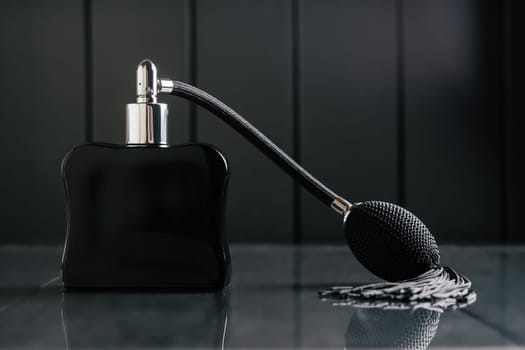 Black bottle of eau de toilette or perfume with long tassel spray pomp stands on dark background on reflective surface. Copy space