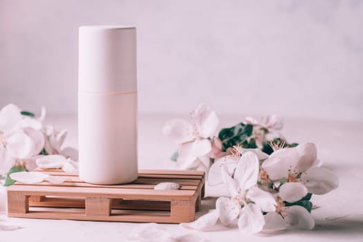 Antiperspirant roll-on deodorant on wooden podium in form of pallet on light plaster surface with apple flowers. Copy space