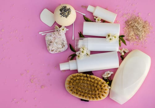 White cosmetic bottles, bath bomb, handmade soap, bath salt, massage brush, sponge, cotton buds with cherry flowers on a pink background. Natural organic cosmetics concept.
