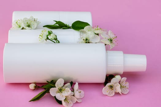 White cosmetic bottles, bath bomb, handmade soap, bath salt, massage brush, sponge, cotton buds with cherry flowers on a pink background. Natural organic cosmetics concept.