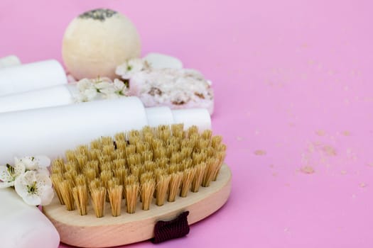 White cosmetic bottles, bath bomb, handmade soap, bath salt, massage brush, sponge, cotton buds with cherry flowers on a pink background. Natural organic cosmetics concept.