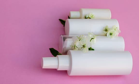 White cosmetic bottles, bath bomb, handmade soap, bath salt, massage brush, sponge, cotton buds with cherry flowers on a pink background. Natural organic cosmetics concept.