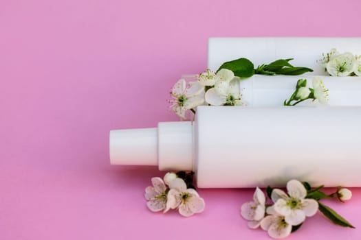 White cosmetic bottles, bath bomb, handmade soap, bath salt, massage brush, sponge, cotton buds with cherry flowers on a pink background. Natural organic cosmetics concept.