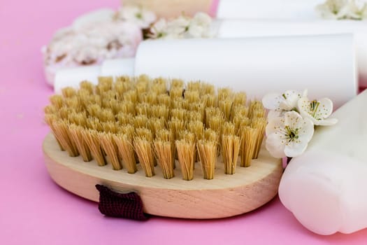 White cosmetic bottles, bath bomb, handmade soap, bath salt, massage brush, sponge, cotton buds with cherry flowers on a pink background. Natural organic cosmetics concept.