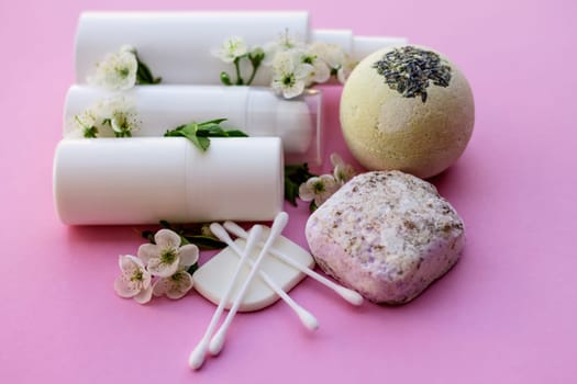 White cosmetic bottles, bath bomb, handmade soap, bath salt, massage brush, sponge, cotton buds with cherry flowers on a pink background. Natural organic cosmetics concept.
