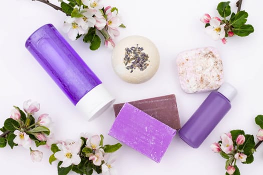 Top view. Lilac cosmetic bottles, bath bomb, handmade soap, bath salt with pear flowers on a white background. Natural organic cosmetics concept. Flat lay
