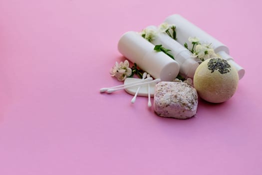 White cosmetic bottles, bath bomb, handmade soap, bath salt, massage brush, sponge, cotton buds with cherry flowers on a pink background. Natural organic cosmetics concept.