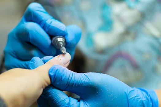 A manicurist in blue gloves makes a manicure with a device, cuticle treatment