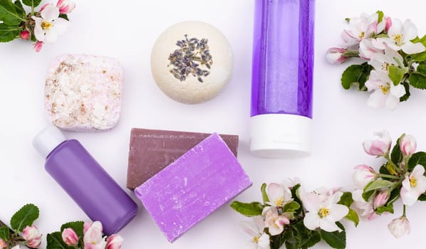 Top view. Lilac cosmetic bottles, bath bomb, handmade soap, bath salt with pear flowers on a white background. Natural organic cosmetics concept. Flat lay