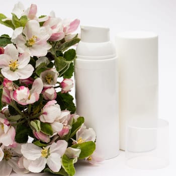 White cosmetic bottles with pear flowers on a white background. Natural organic cosmetics concept