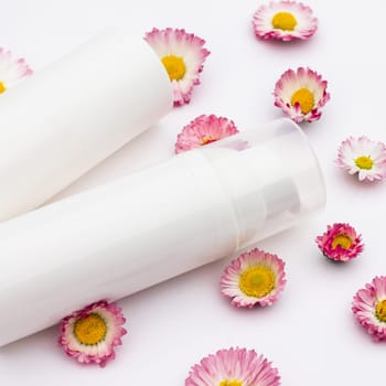 White cosmetic bottles with daisy flowers on a white background. Natural organic cosmetics concept