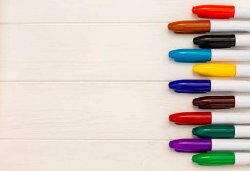 Multi-colored markers on a white wooden background. Top view. Copy space