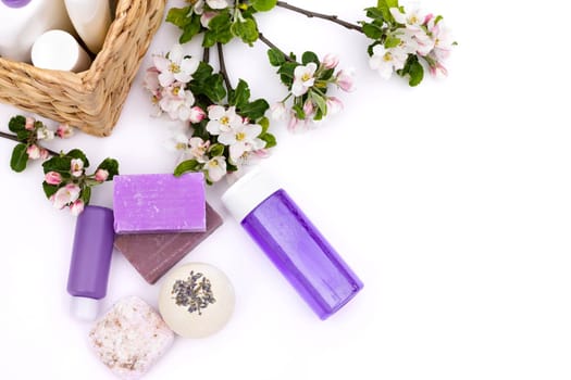 Lilac cosmetic bottles, bath bomb, handmade soap, bath salt near wicker basket with pear flowers on a white background. Natural organic cosmetics concept. Flat lay