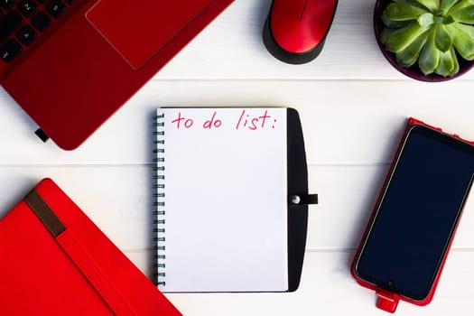 Notebook with To Do List with phone, red diary and laptop on a white wooden background. Top view. Copy space
