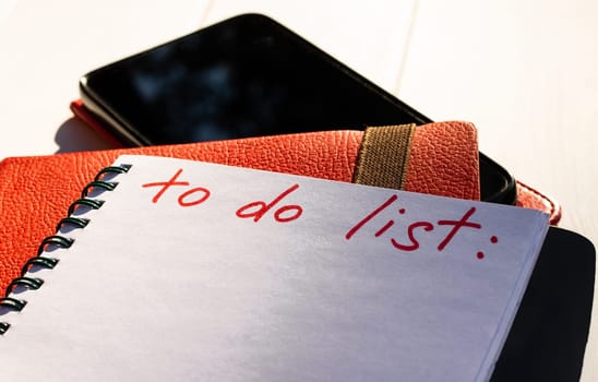 Notebook with To Do List with phone and red diary on a white wooden background. Copy space