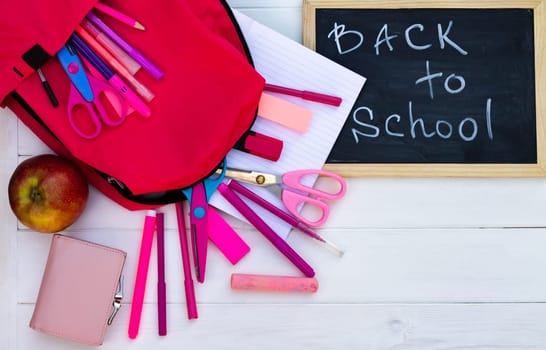 Back to school black chalk board on a white wooden background, pink supplies. Top view. Copy space. Education concept.