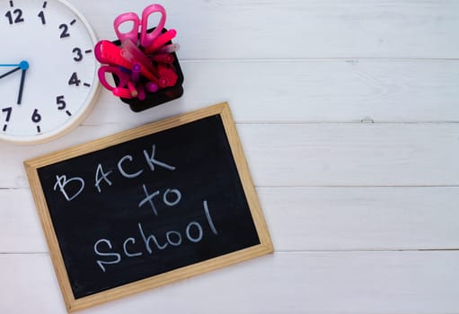 Back to school black chalk board on a white wooden background, pink supplies. Top view. Copy space. Education concept.