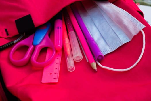 Pink school supplies and medical mask in a pink backpack. Education, back to school concept.