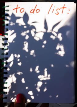 Notebook with To Do List with blurred plant shadow. Copy space