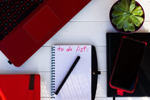 Notebook with To Do List with phone, red diary and laptop on a white wooden background. Top view. Copy space