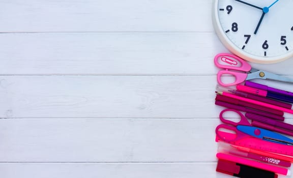 Pink school supplies and clock on a white wooden background. Top view. Copy space. Education and back to school concept.