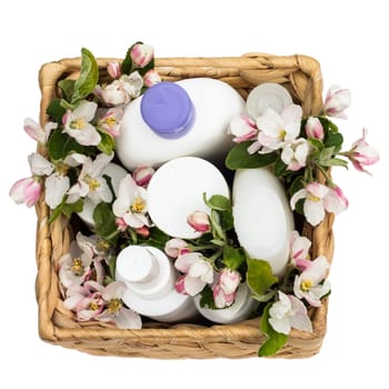 White cosmetic bottles in a wicker basket with pear flowers isolated on a white background. Natural organic cosmetics concept. Top view