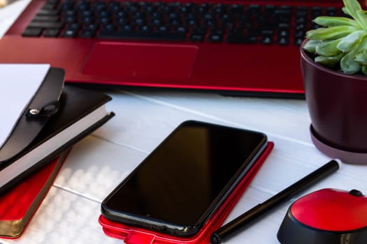 Red mobile phone, diary and laptop on a white wooden background