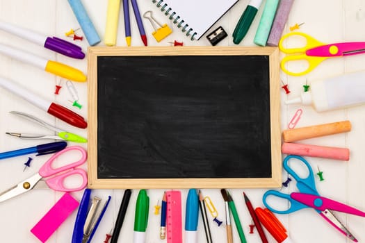 Back to school black chalk board on a white wooden background, color supplies. Top view. Copy space. Education concept.