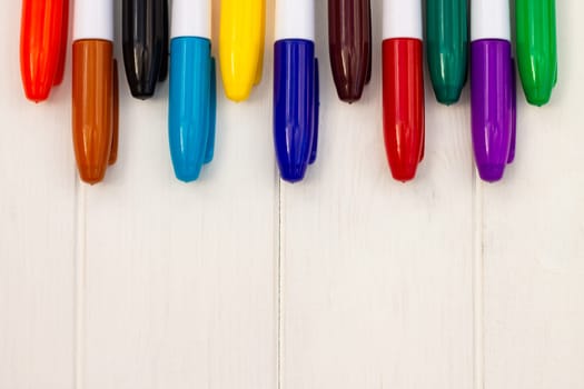 Multi-colored markers on a white wooden background. Top view. Copy space