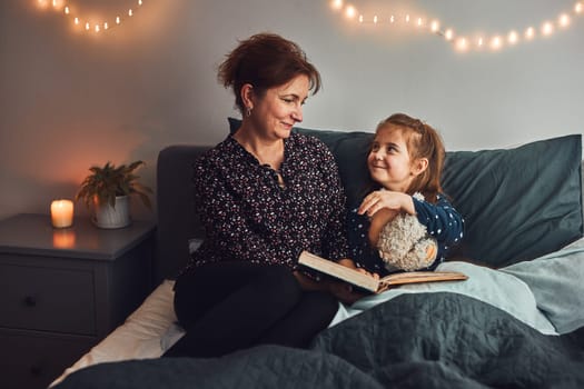 Mother reading book her daughter in bed before going to sleep. Reading stories before sleep. Bedtime stories for child